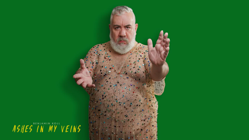 A person with a beard wearing a patterned shirt stands against a green background with arms extended. Text in the bottom left corner reads "ASHES IN MY VEINS."